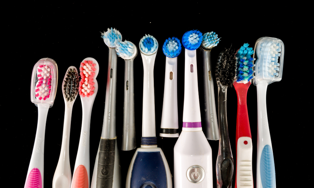Row of manual and electric toothbrushes with different brush head designs on black background